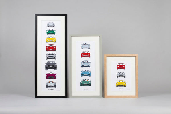 Three framed vertical art prints featuring stylized car illustrations in different colors, displayed on a white wall in a home interior next to a wooden door and staircase railing.