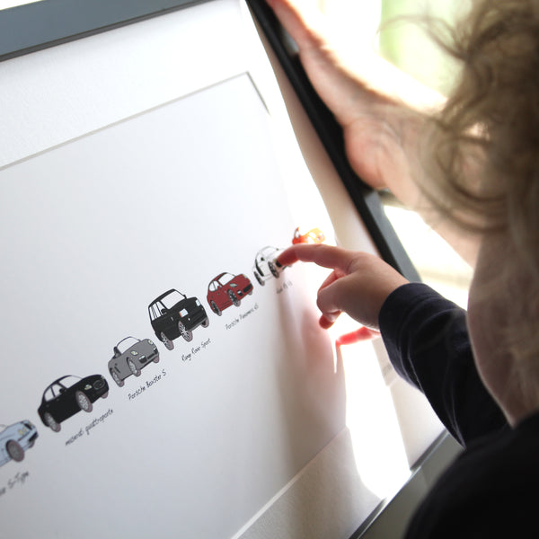Pointing at artwork. Artwork includes persons car history. Maserati. Range Rover sport. Porsche Boxster S. Your life in cars framed artwork. child pointing at dads bespoke artwork.