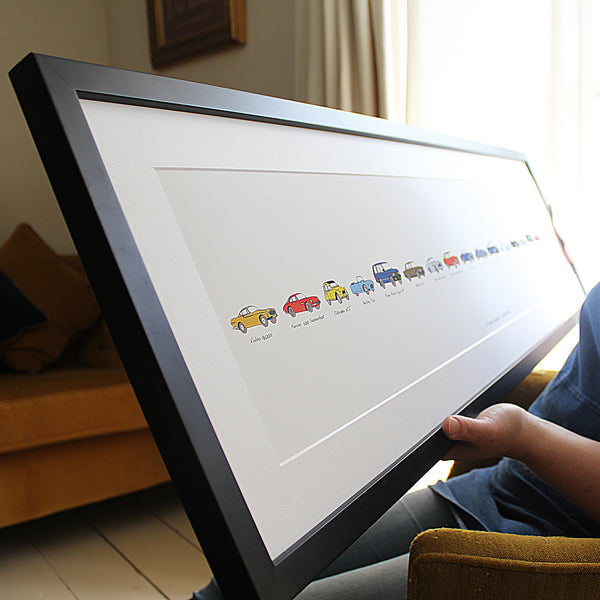 Person holding a Personalised car Artwork in a frame. Automobile framed artwork. my life in cars. Volvo p1800. Range Rover Classic. Citroen 2CV. Ferrari 500 Superfast. berkeley t60. range rover vogue. car artwork gift. Framed artwork, personalised car artwork, my life in cars gift, bespoke car gift, my first car, my life in cars